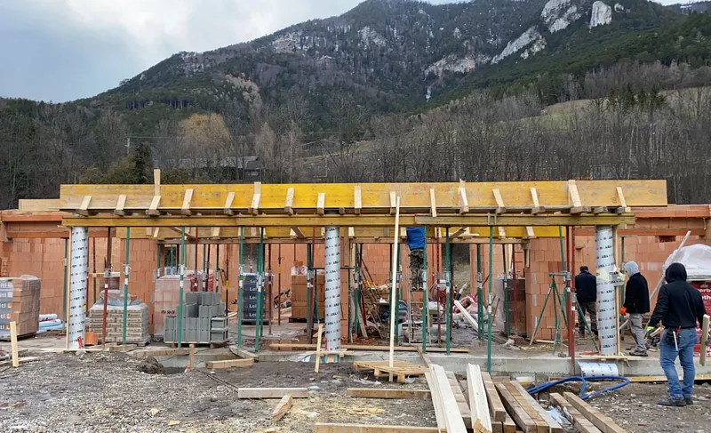Ziegelrohbau mit Stützen und Arbeitern vor Bergpanorama