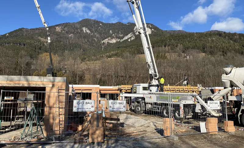 Betonpumpe beim Betonieren eines Ziegelrohbaus vor Bergkulisse